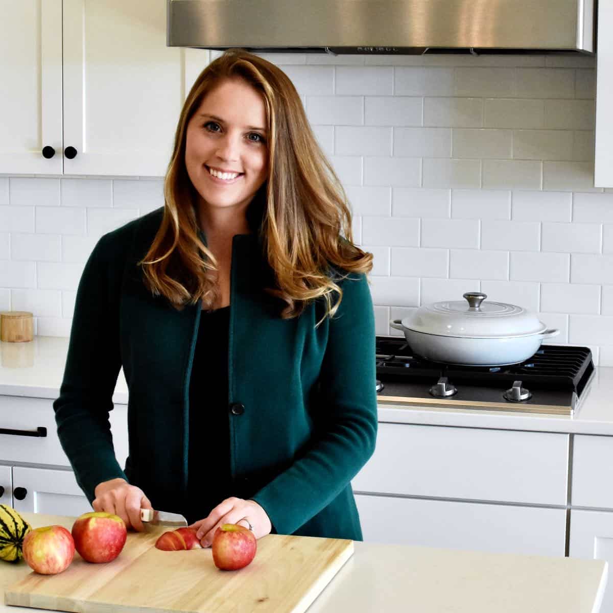 A woman wearing a green blazer chopping an apple on a cutting board.