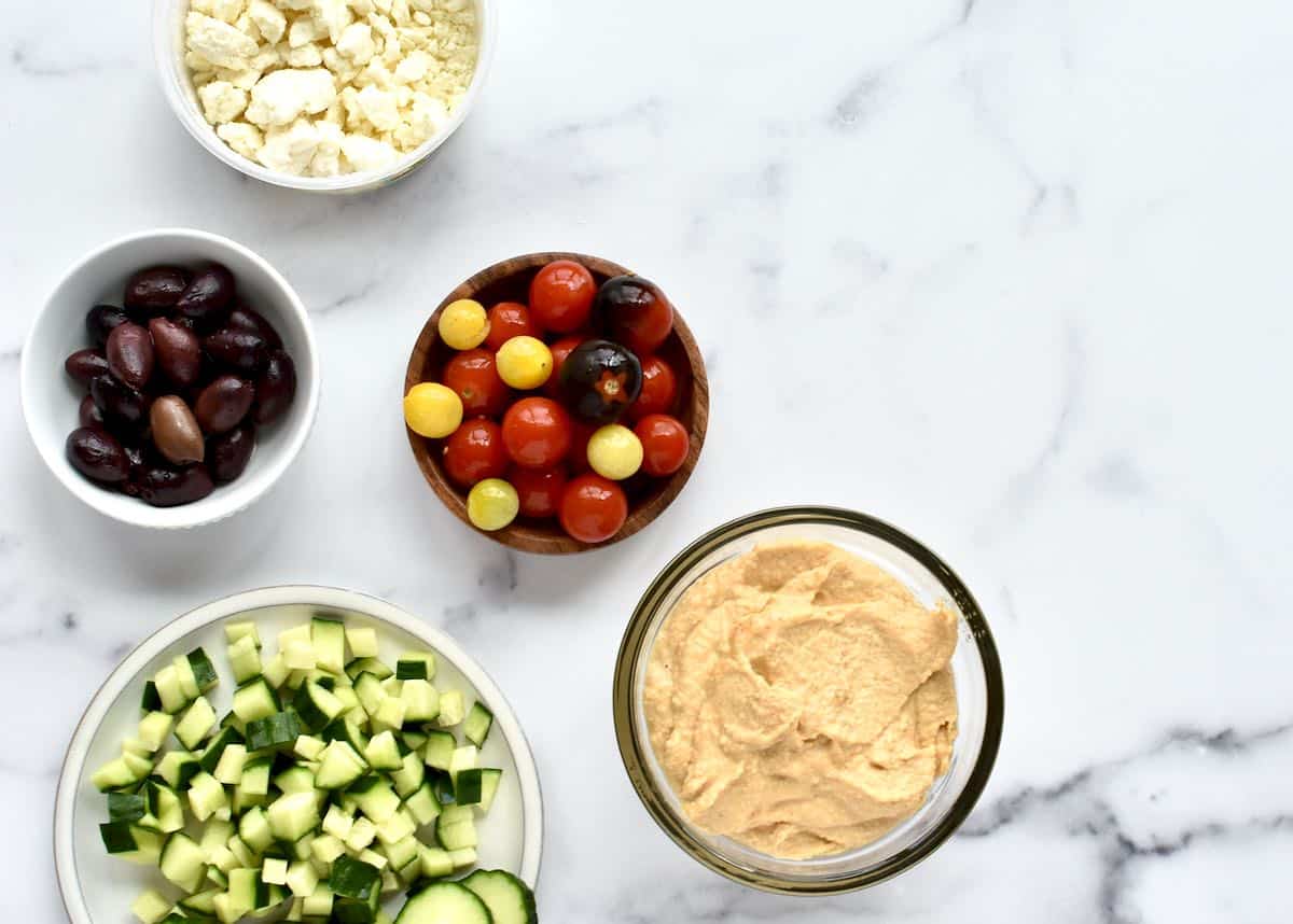 Ingredients for loaded hummus platter including hummus, cucumber, tomatoes, olives and feta cheese