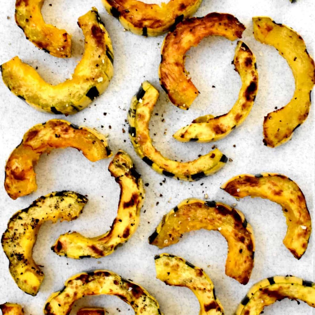 Grilled golden brown squash half moons on a white background, sprinkled with salt and pepper.