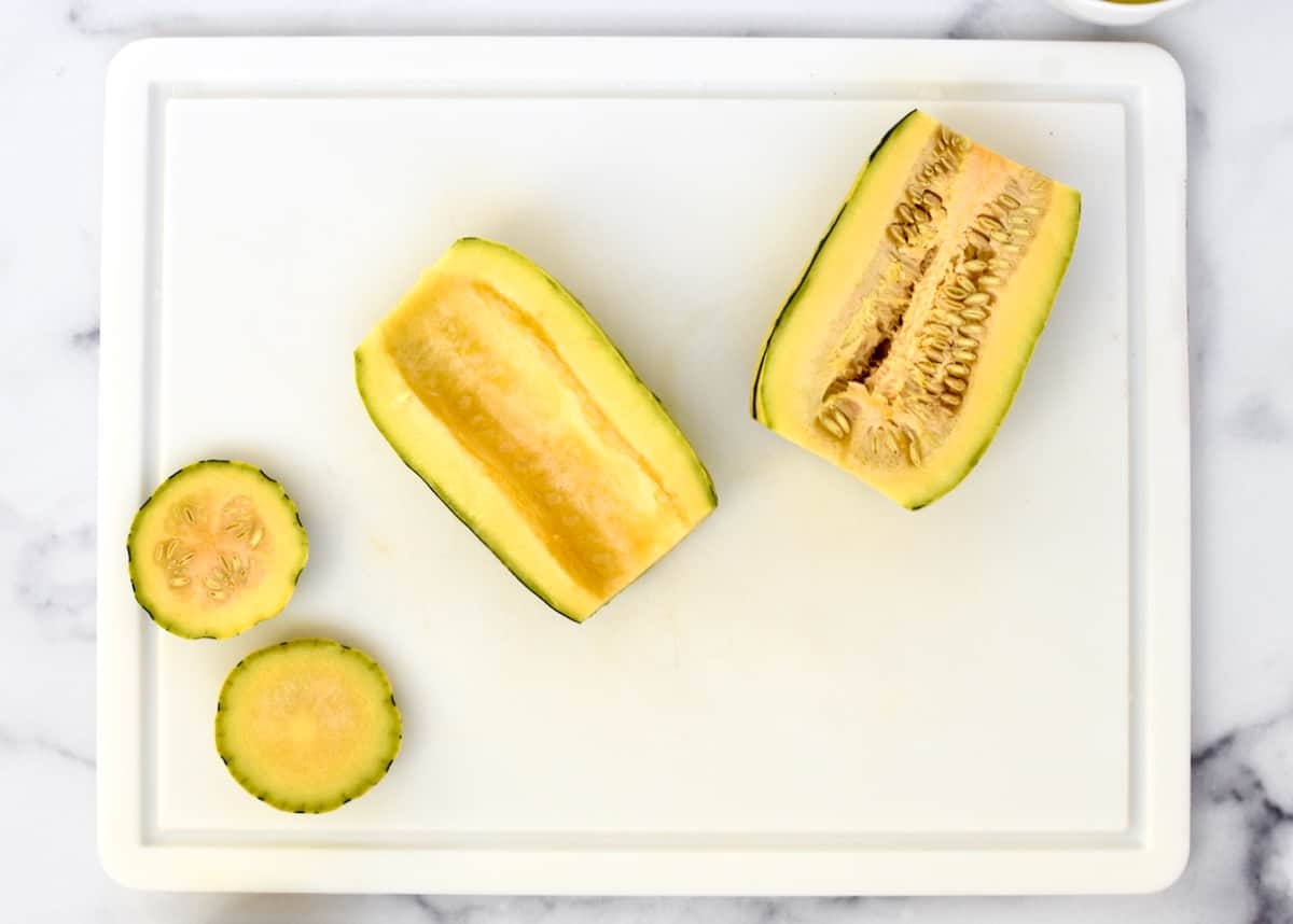 A white cutting board with two halves of delicata squash, one with seeds and one without. 