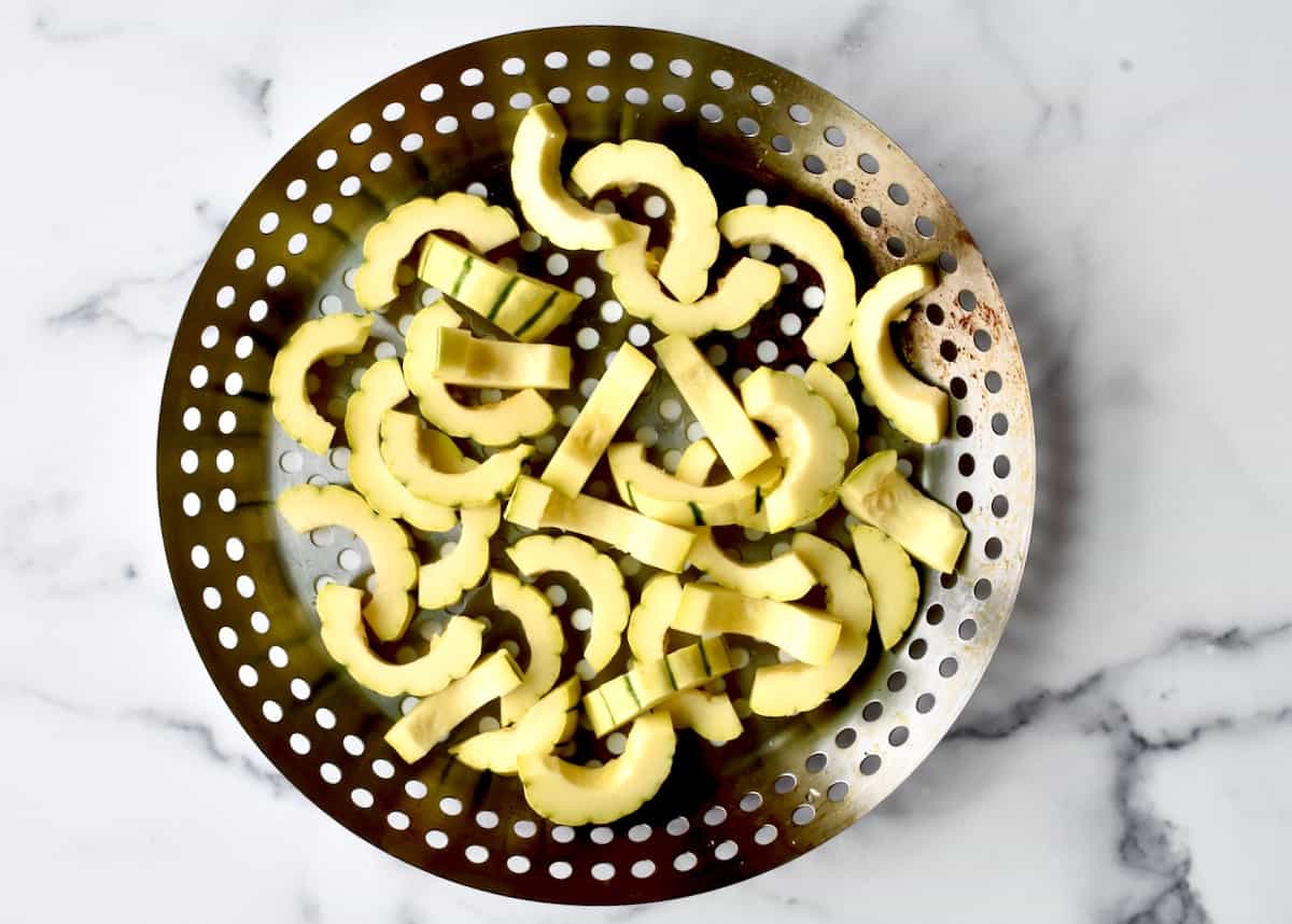 A grill wok with slices of delicata squash. 