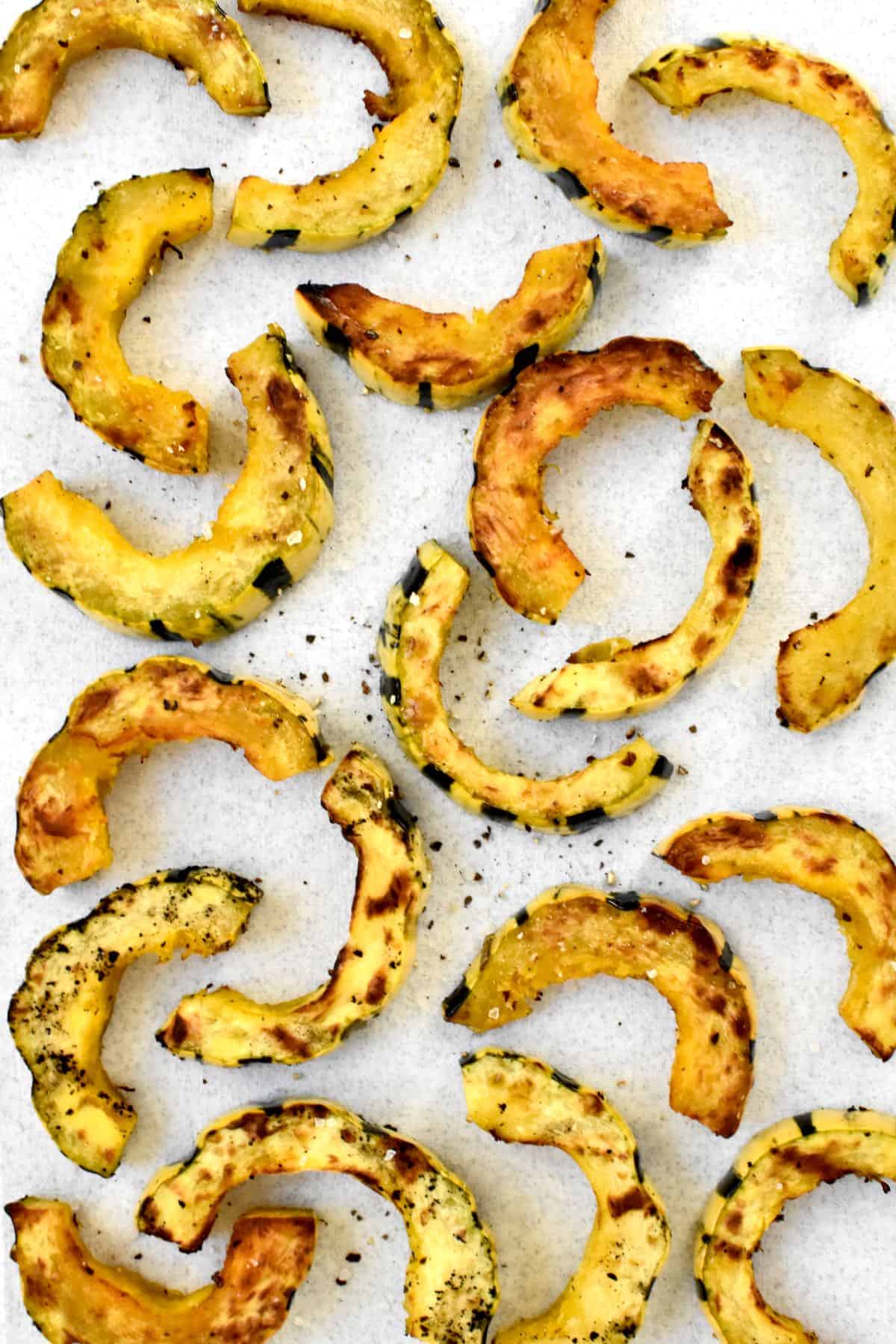 Grilled golden brown squash half moons on a white background, sprinkled with salt and pepper.