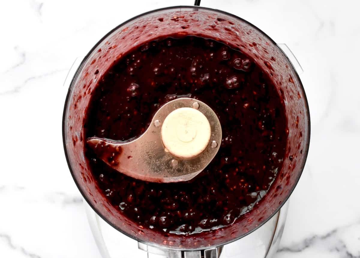 The bowl of a food processor with blended blackberries. 