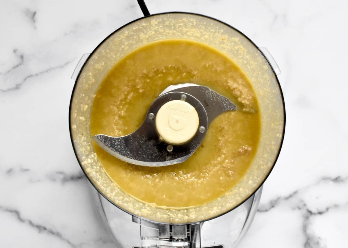 The bowl of a food processor with blended lemon, olive oil and cheese.