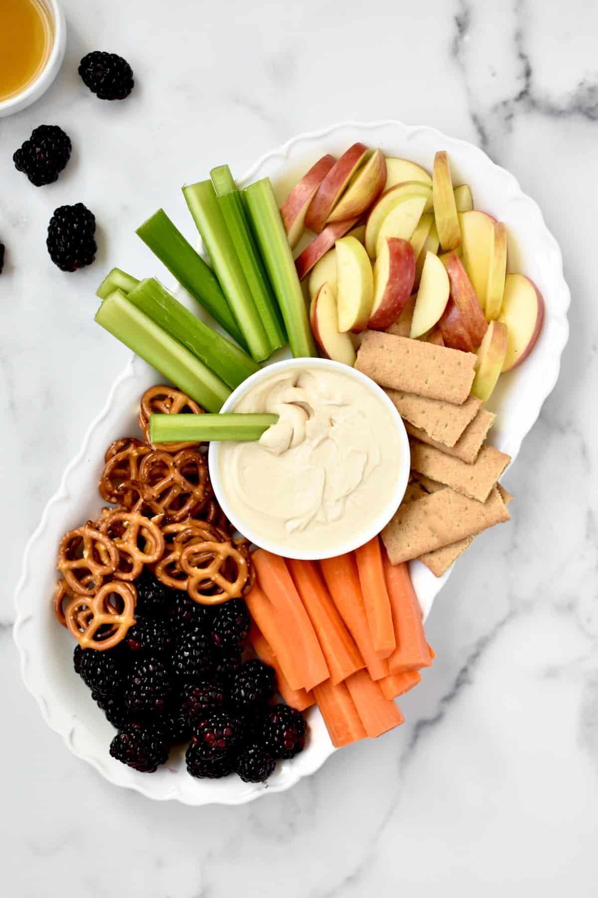 A platter with veggies, fruits, pretzels, graham crackers and peanut butter greek yogurt dip. 