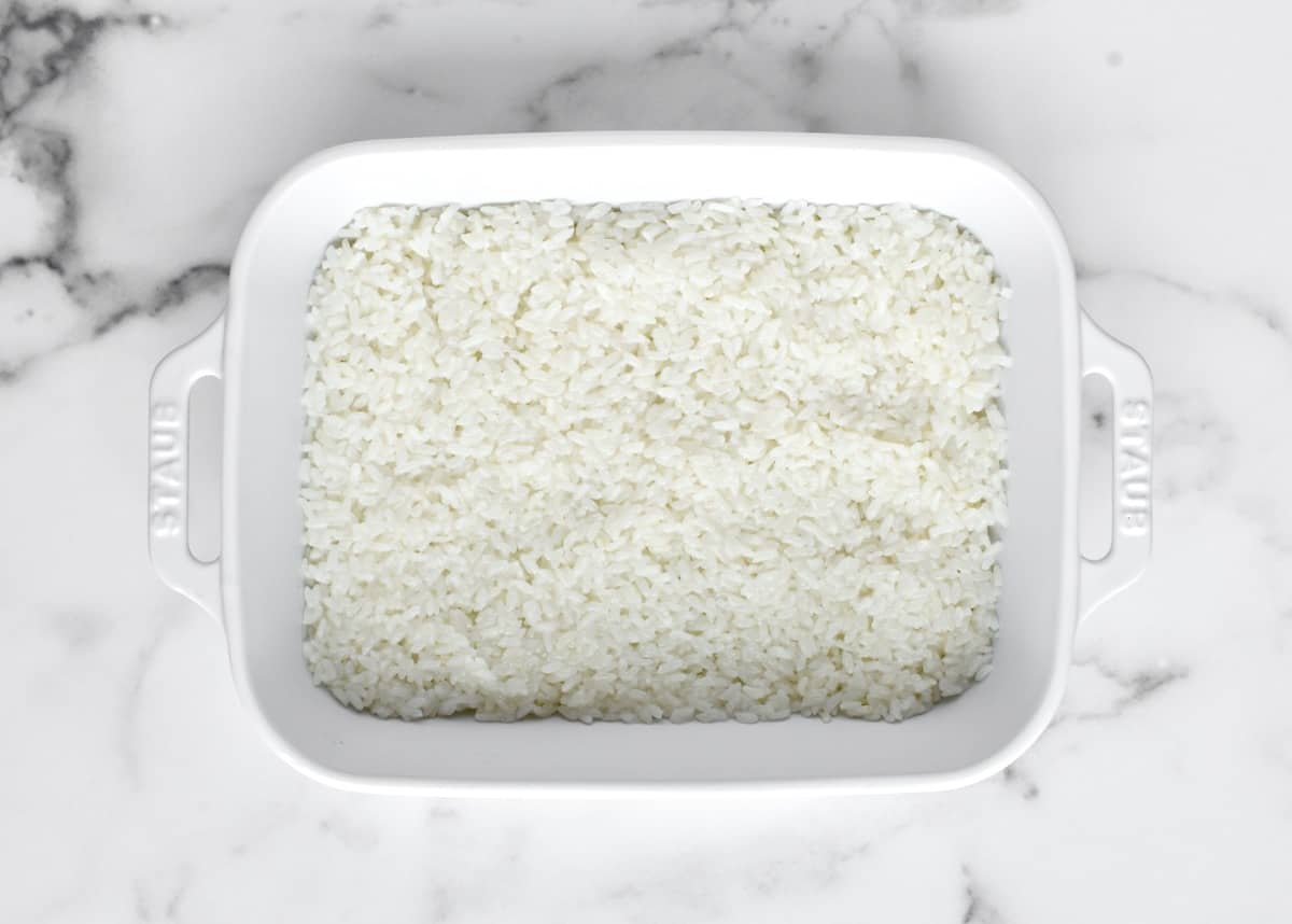 A white casserole dish with a layer of white sushi rice. 