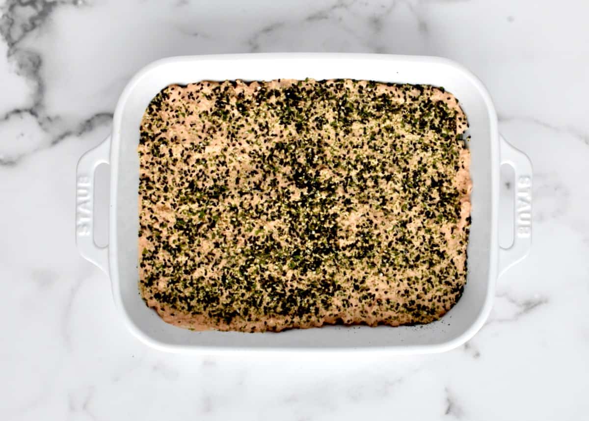 A white casserole dish with a layer of spicy salmon mixture covered in furikake.