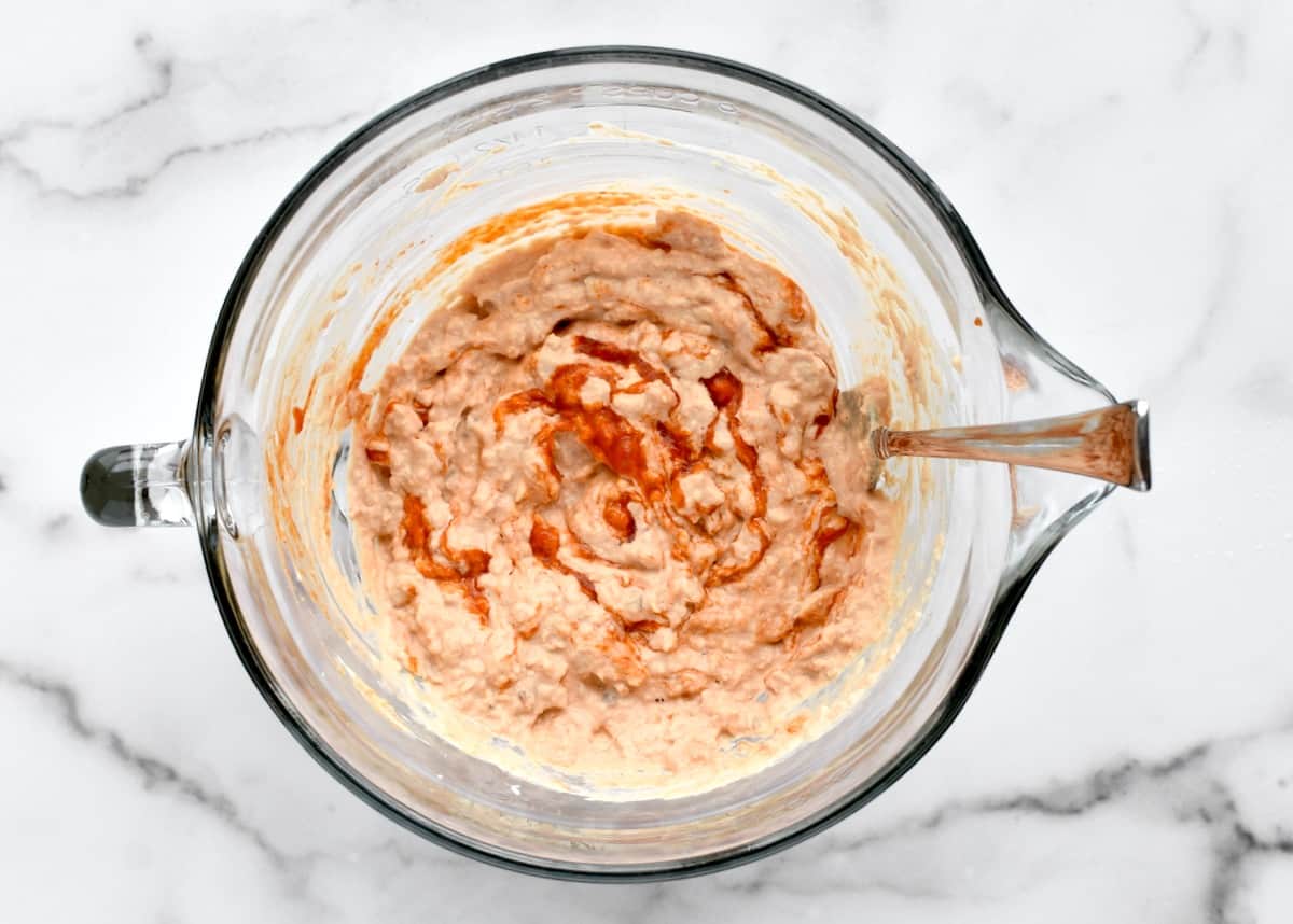 A large glass bowl with spicy mayo and salmon being mixed with a spoon.