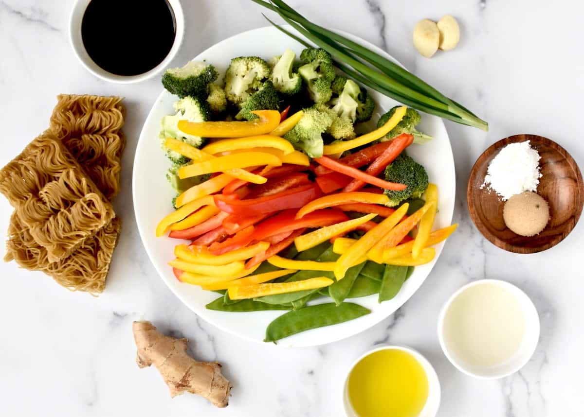 Ingredients for veggie brown rice ramen stir fry, including noodles, ginger, garlic, soy sauce, olive oil, vinegar, brown sugar, cornstarch, and chopped fresh veggies.