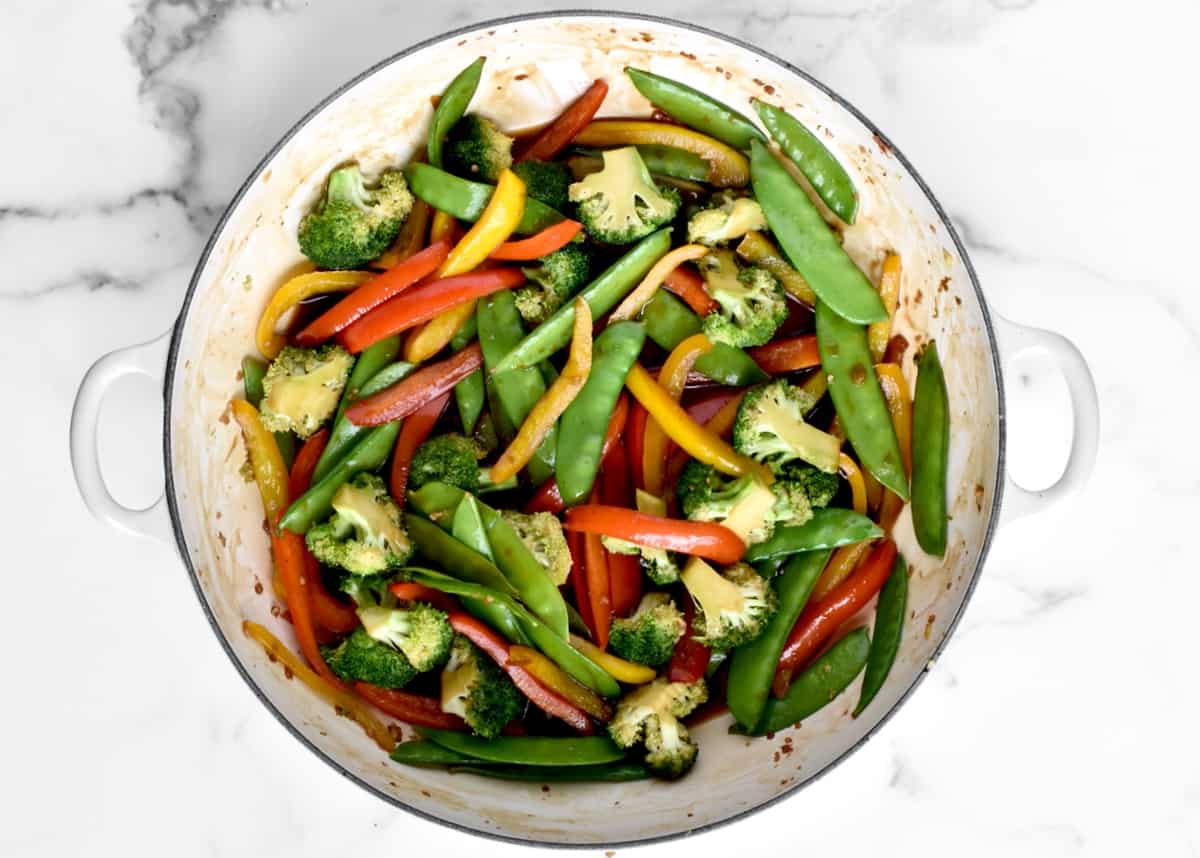 A large skillet with stir fried veggies in brown stir fry sauce.