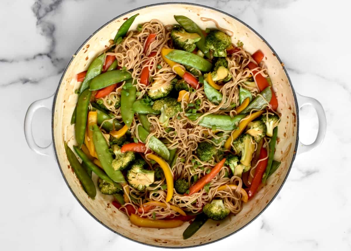 A large skillet with stir fried veggies and ramen noodles in brown stir fry sauce. 