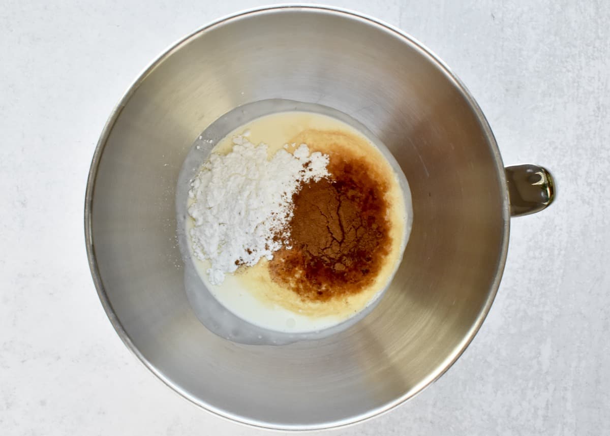 The stainless steel bowl of a stand mixer with ingredients for pumpkin spice whipped cream, not yet combined.