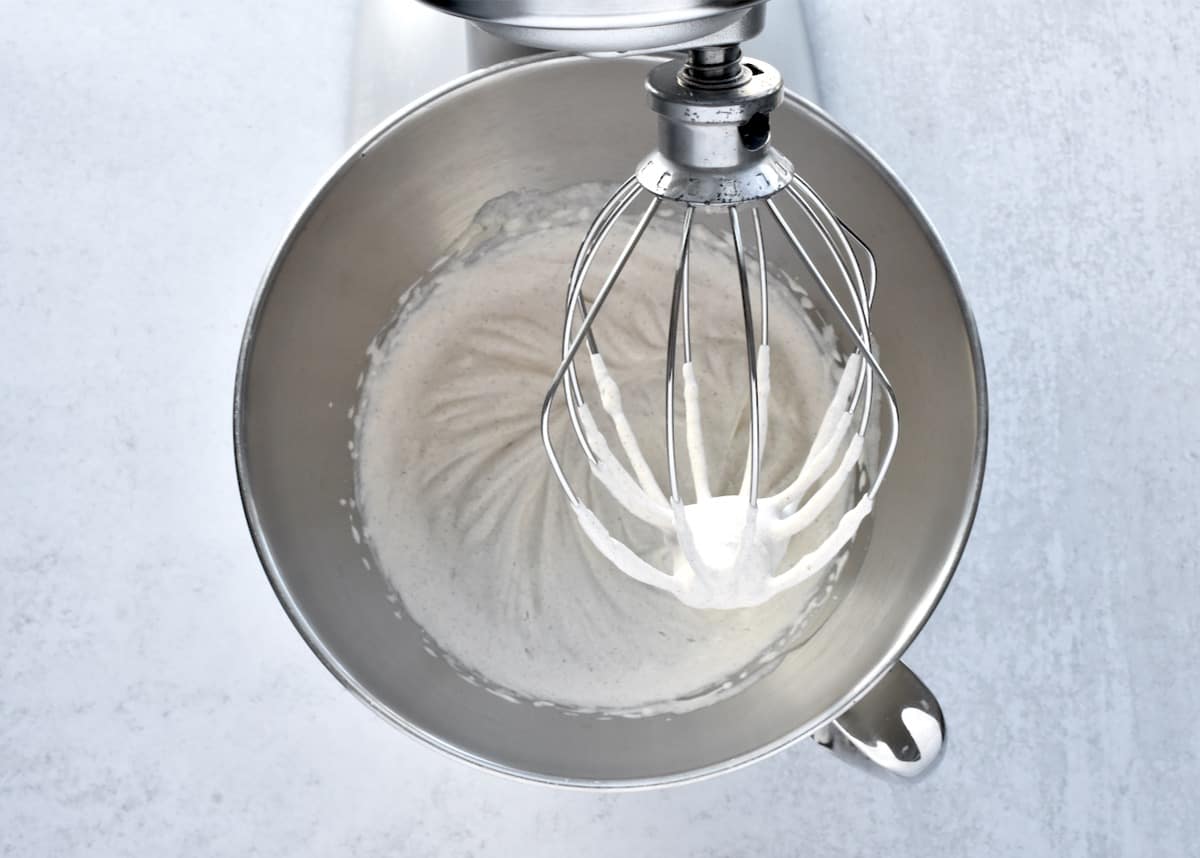 The stainless steel bowl of a stand mixer with cream at soft peaks.