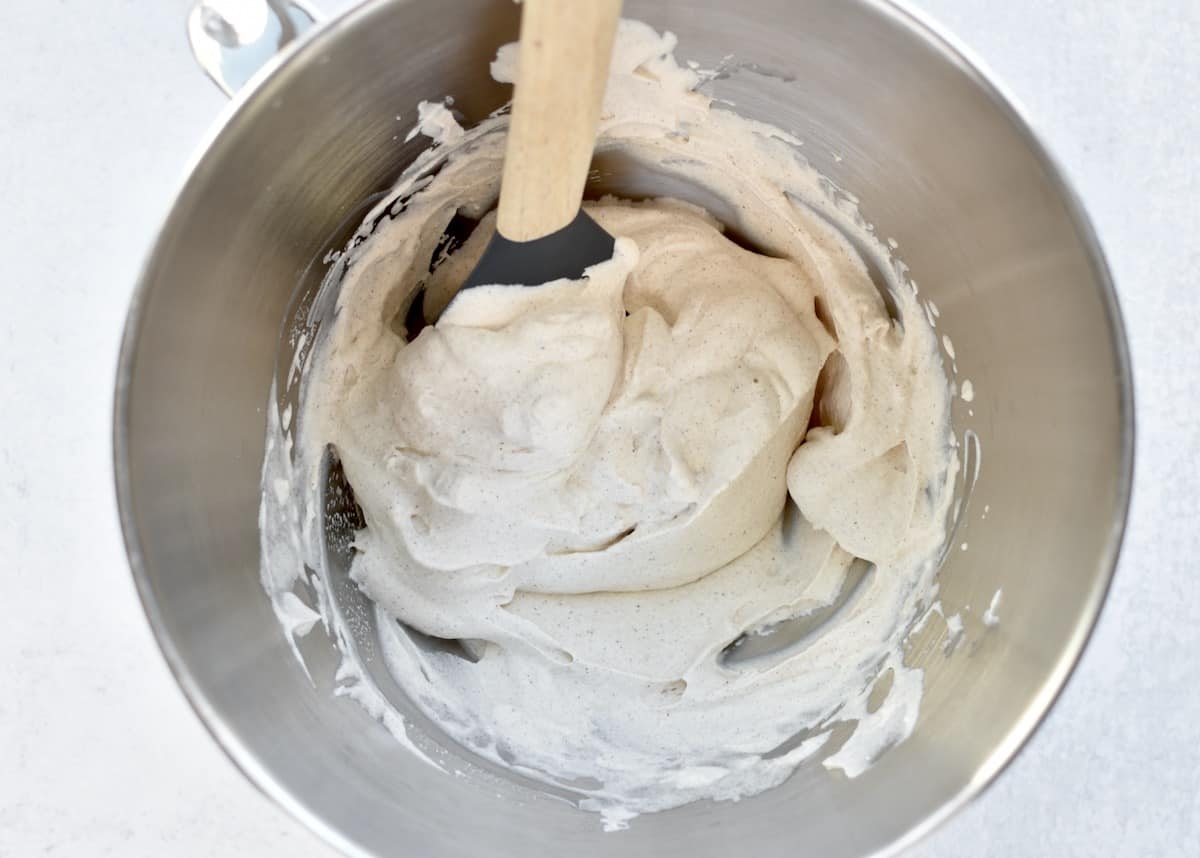 The stainless steel bowl of a stand mixer showing whipped cream at medium peaks with soft, foldable texture.