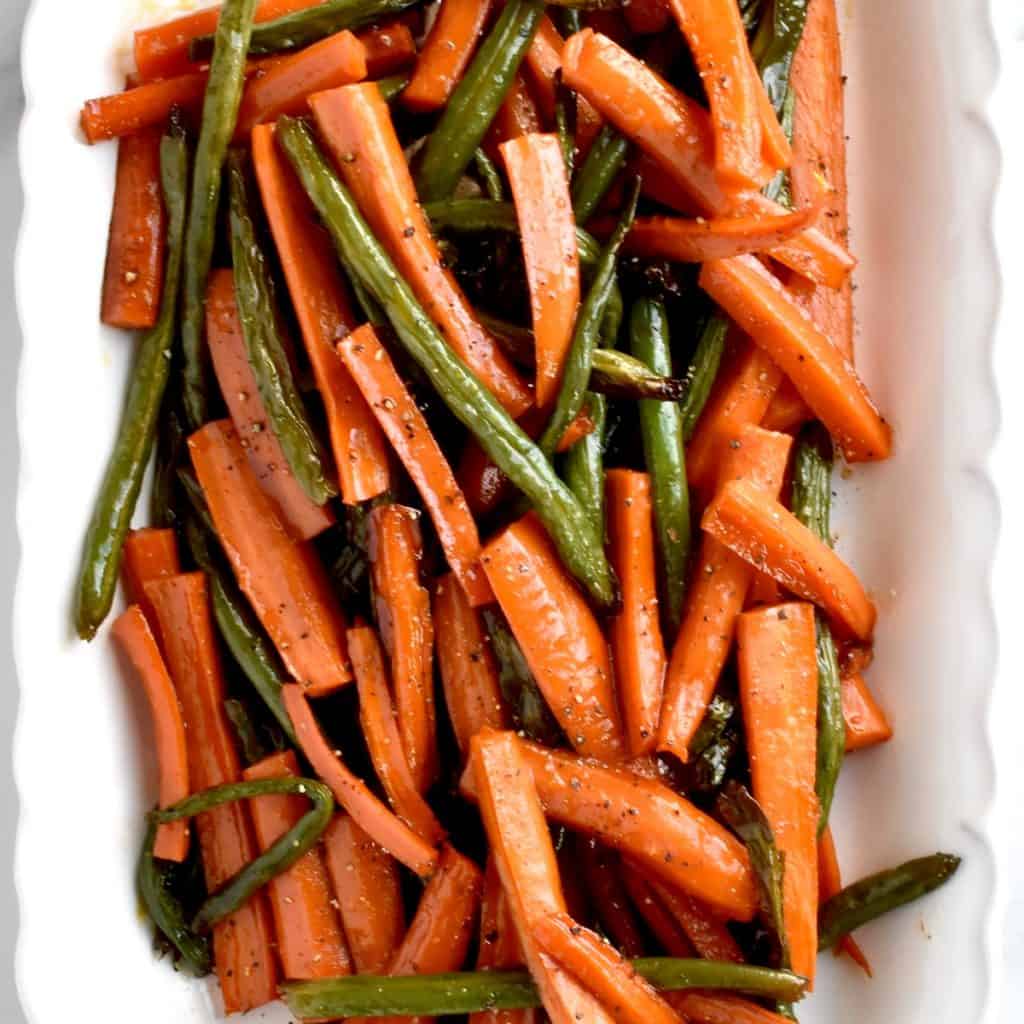 a close up shot of honey roasted carrots and green beans with a white background.