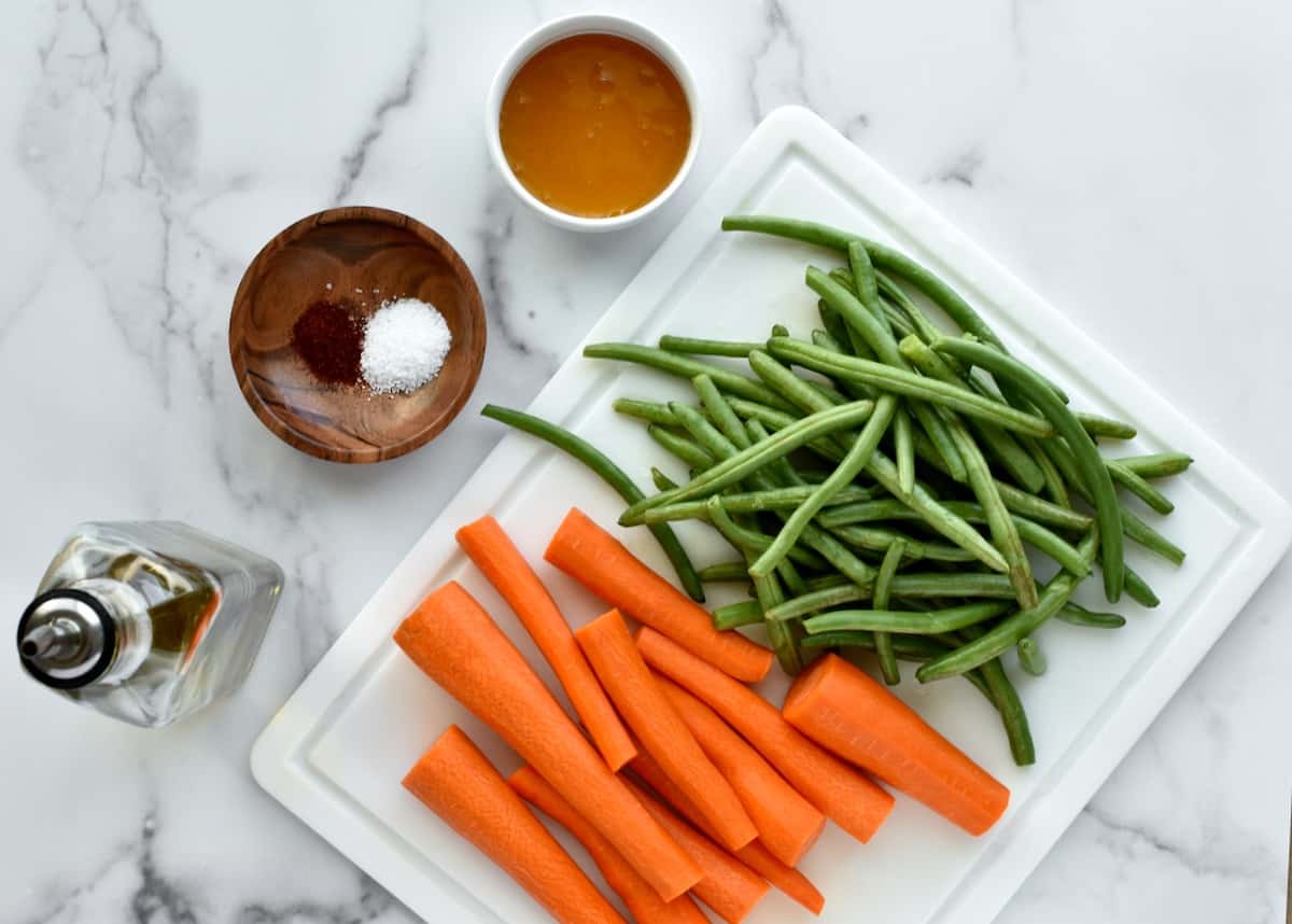 ingredients for roasted carrots and green beans on a marble background.