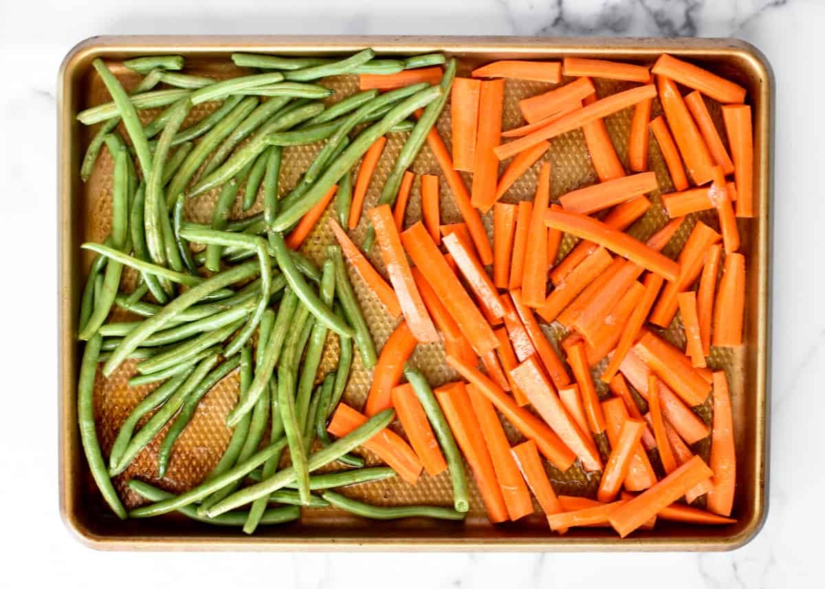 a sheet pan with carrots and green beans, not yet cooked.