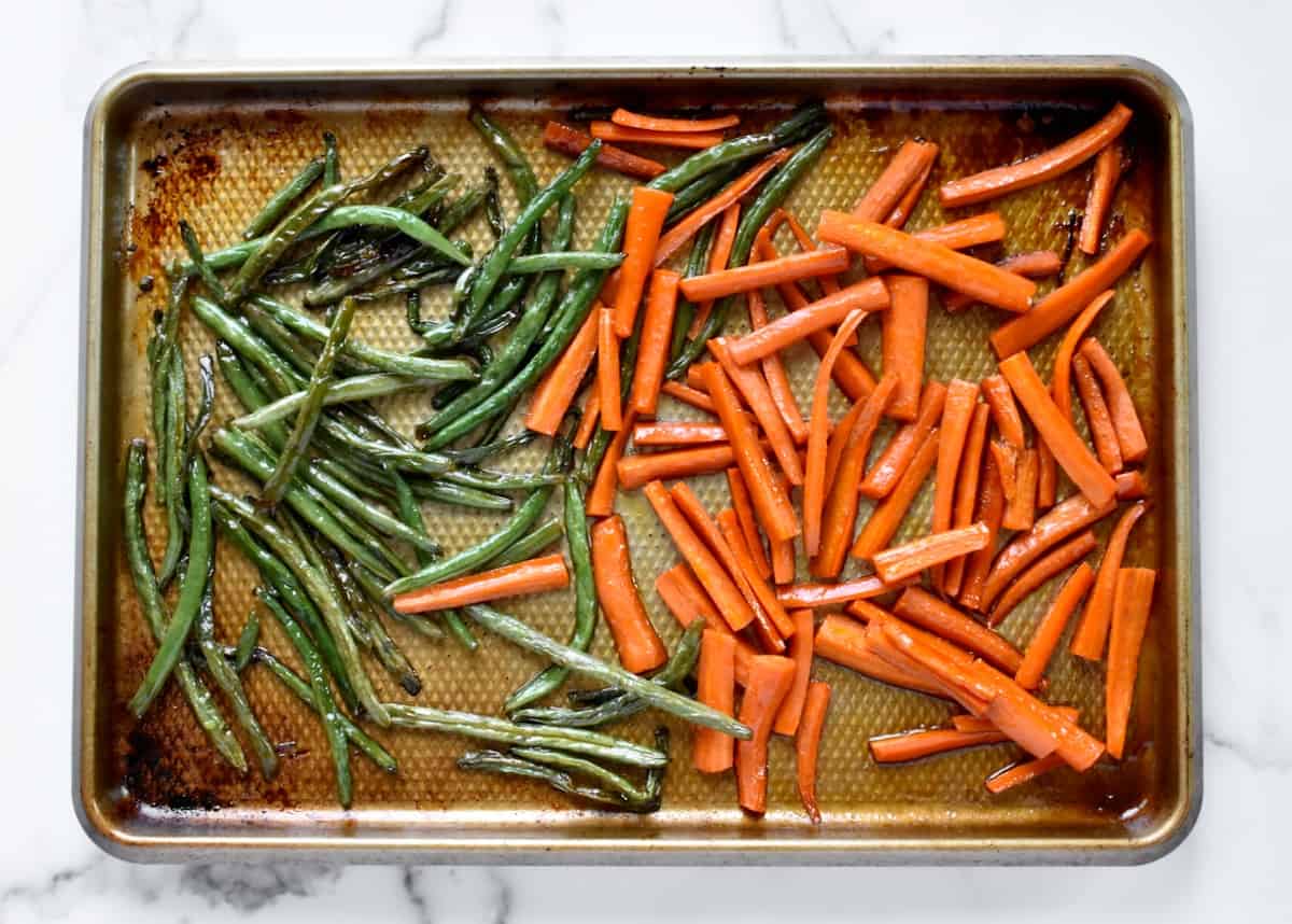 a sheet pan with carrots and green beans, roasted and caramelized.