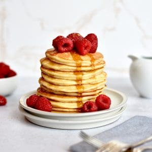 a stack of pancakes on top of two plates, with syrup drizzling down the side of the pancake stack.