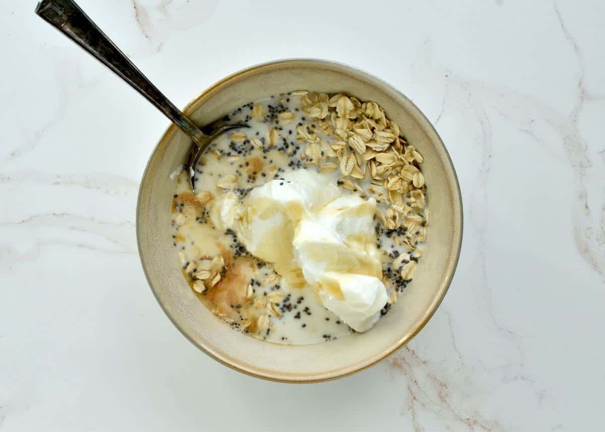 A grey bowl on a marble background with all the ingredients for overnight oats combined but not yet stirred.