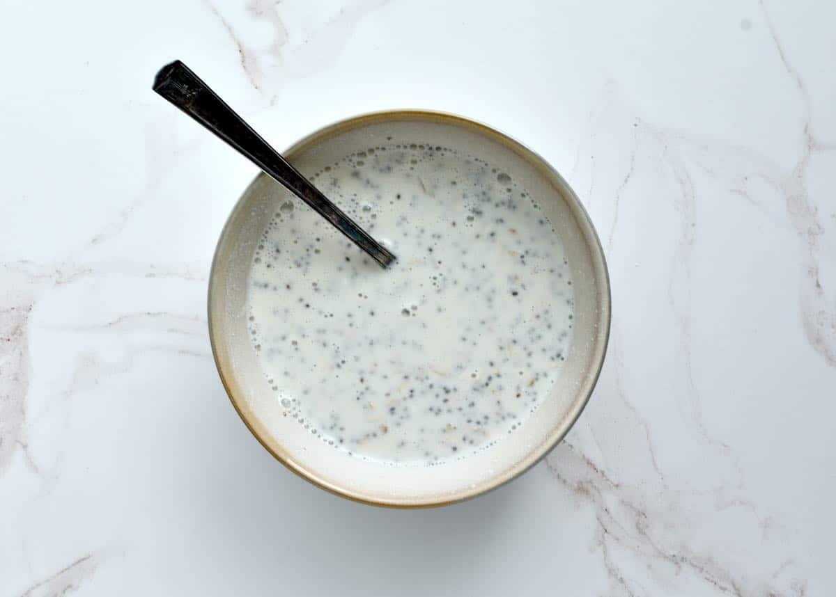 A grey bowl on a marble background with stirred overnight oats.