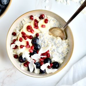 A grey bowl of vanilla overnight oats on a marble background, garnished with banana, berries, coconut and pomegranate seeds.