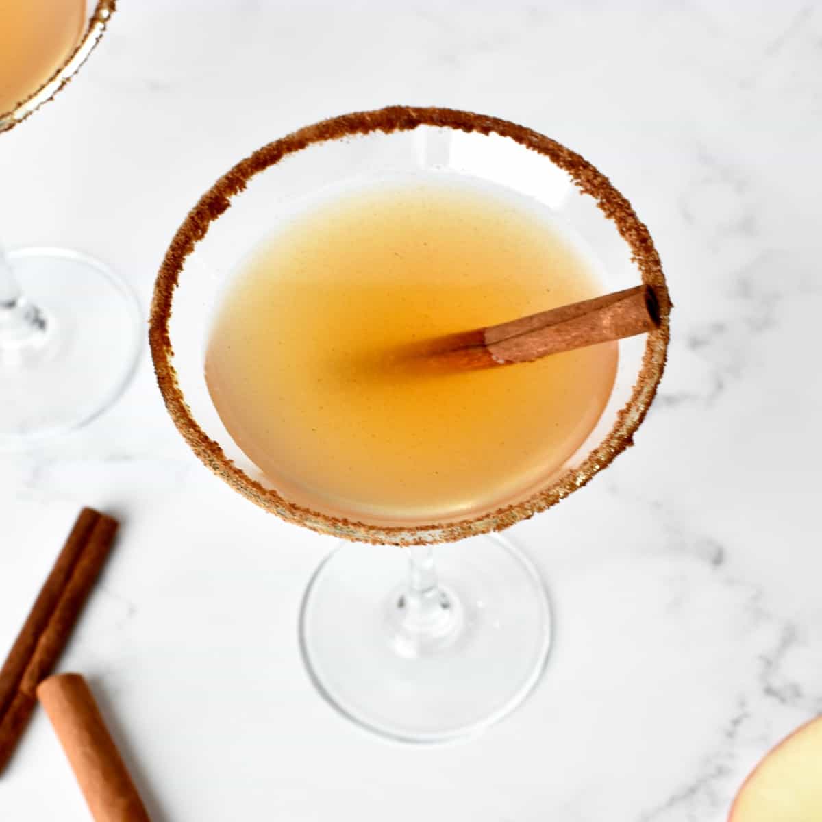 An apple cider martini garnished with a cinnamon stick on a marble background.