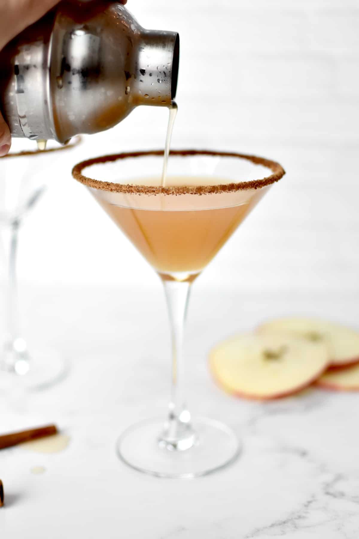 An martini glass with a hand straining martini from a shaker into the glass.