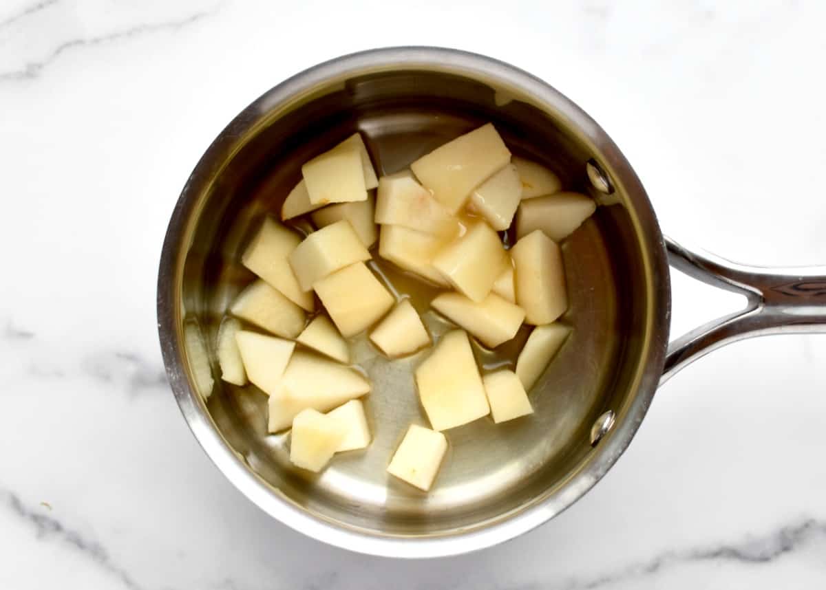 A stainless steel pot with diced pears on a marble background.