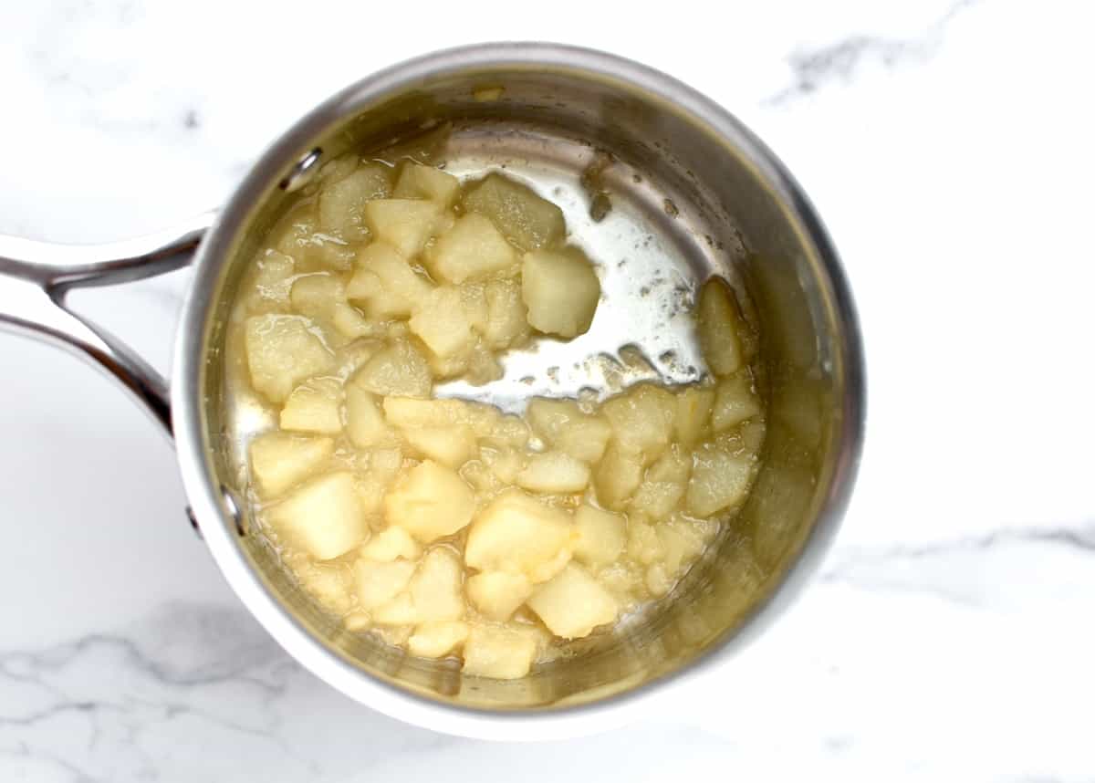 A stainless steel pot with sauteed pears on a marble background. The pears are soft and breaking down.