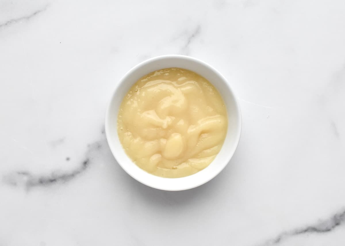 A white bowl of creamy pear sauce on a marble background.