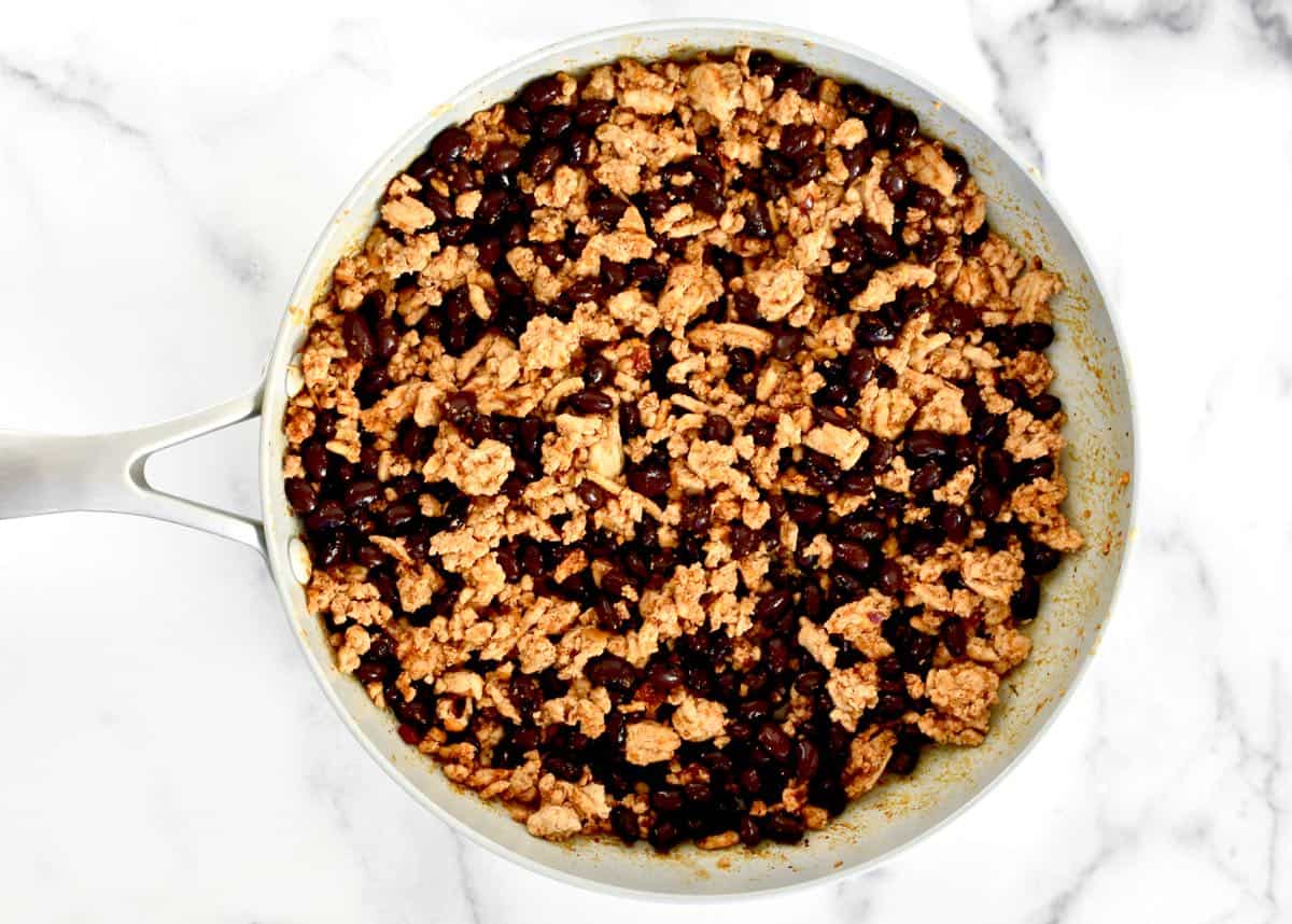 A large grey skillet on a marble background. The skillet contains a meat and black bean mixture with taco seasoning.