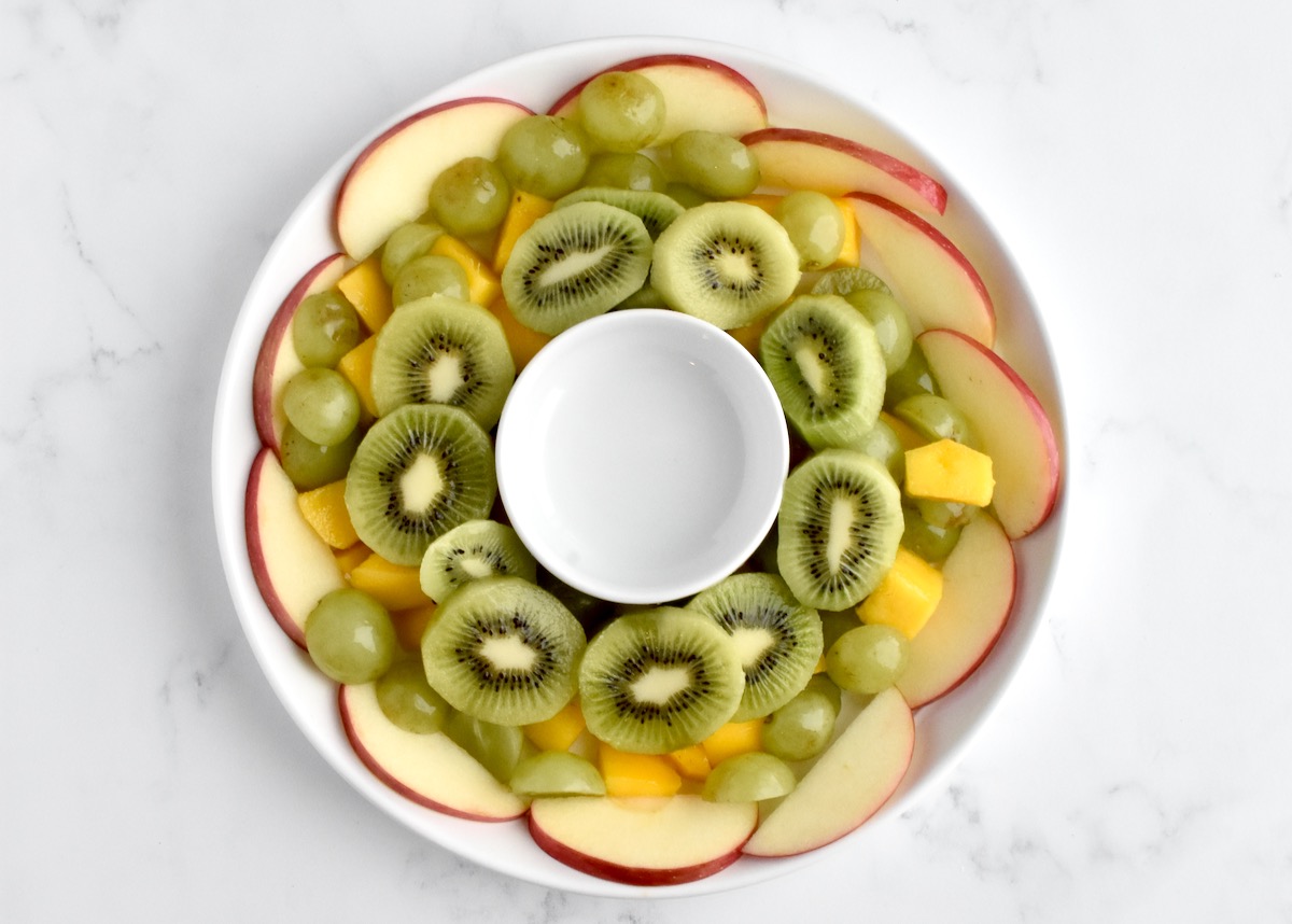 The second layer of a fruit salad, with kiwis and apples framing the wreath shape.