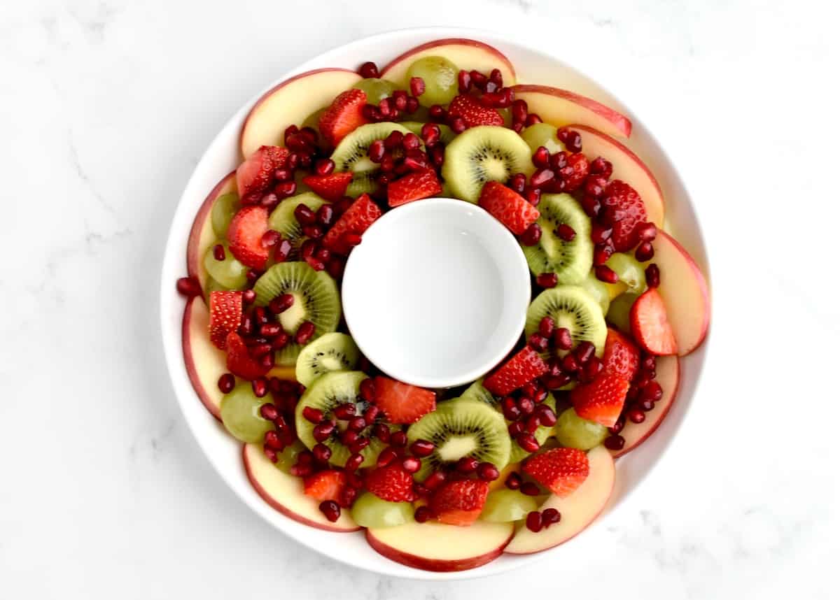 The final layer of the fruit salad, with pomegranate seeds sprinkled on top of the wreath shaped fruit.