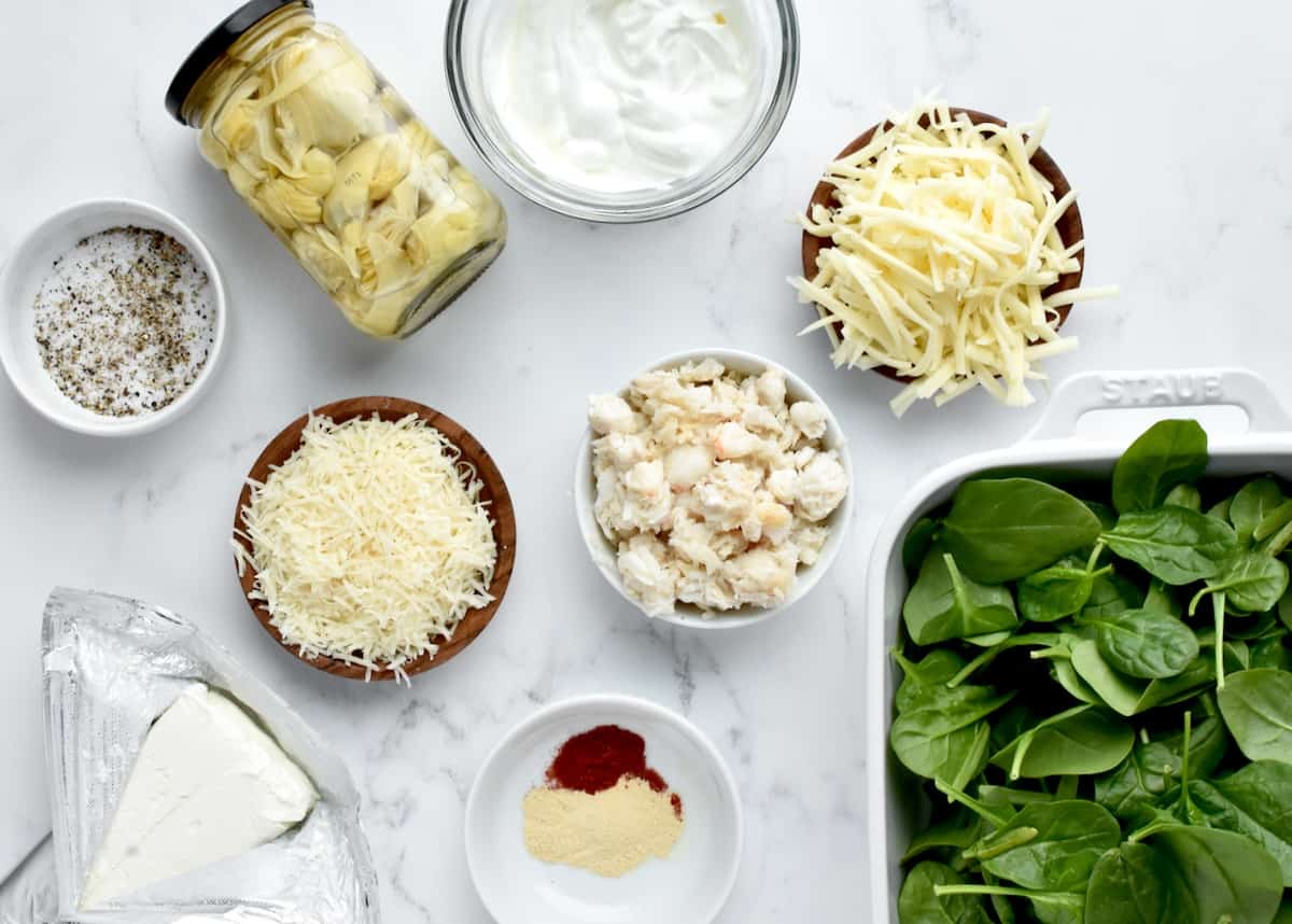 Ingredients for crab spinach artichoke dip on a marble background.