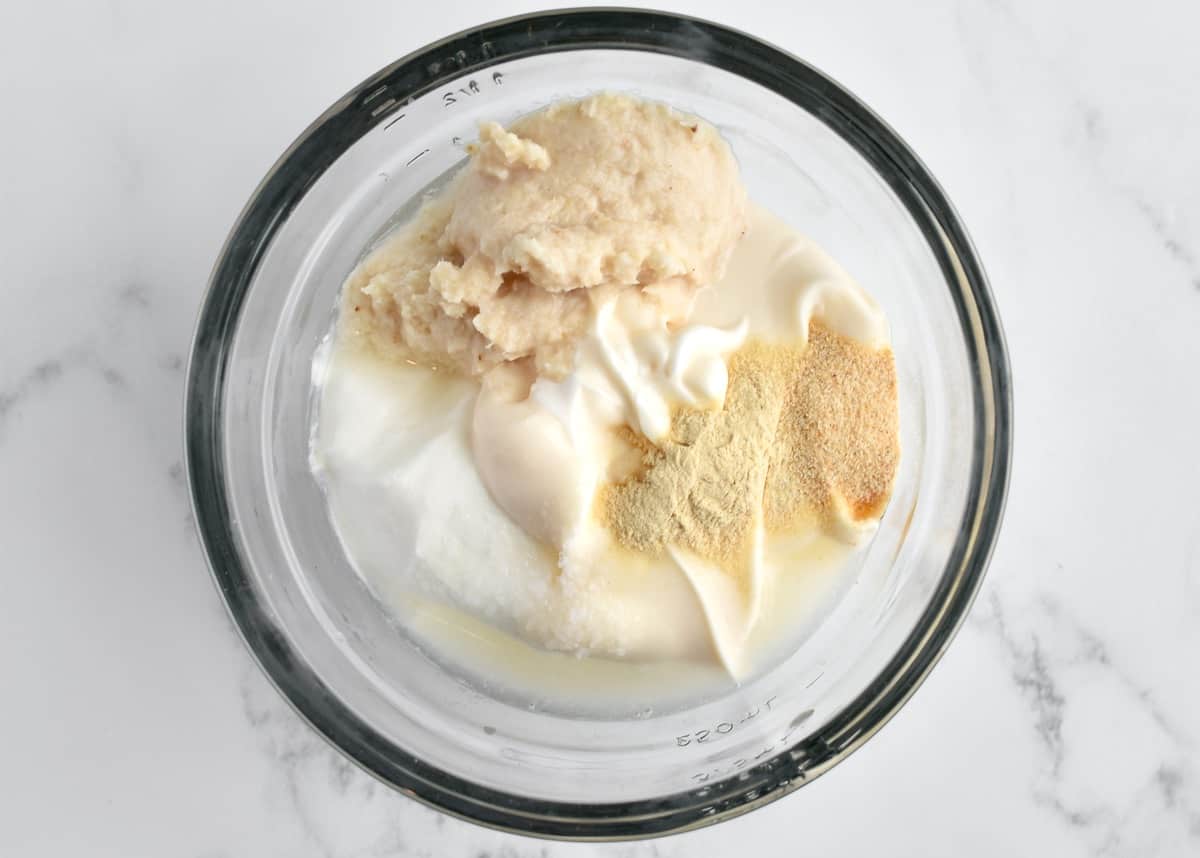 A glass bowl with ingredients for horseradish aioli on a marble background.