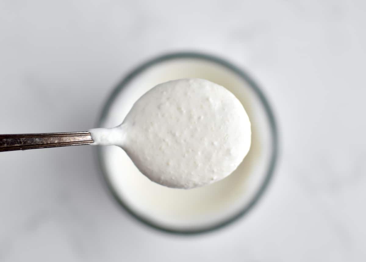 A closeup of a spoon with a spoonful of horseradish aoili, with a bowl of aioli blurred in the background.