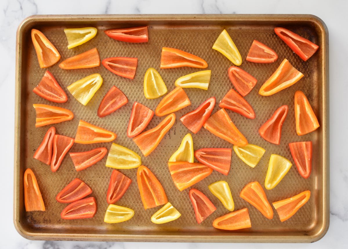 A sheet pan on a marble background. The sheet pan contains halved mini peppers.