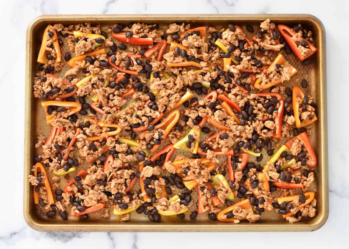 A sheet pan on a marble background. The sheet pan has mini peppers with meat and beans.