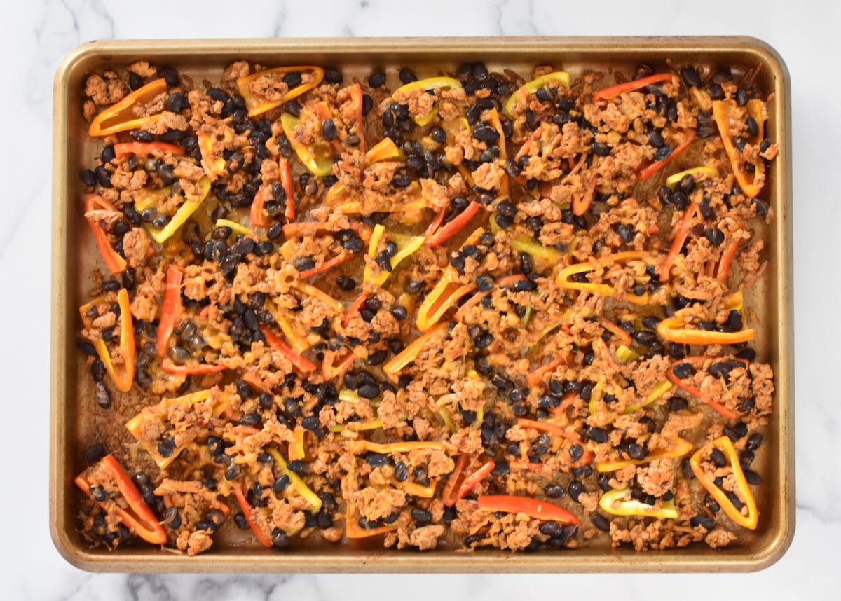 A sheet pan on a marble background. The sheet pan has cooked mini peppers with meat and melted cheese.