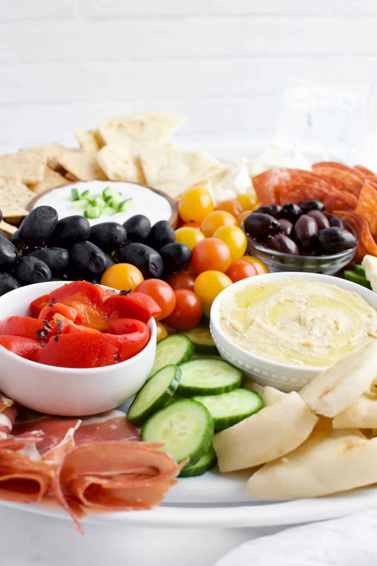 A side view of a Mediterranean charcuterie board against a white brick backsplash.