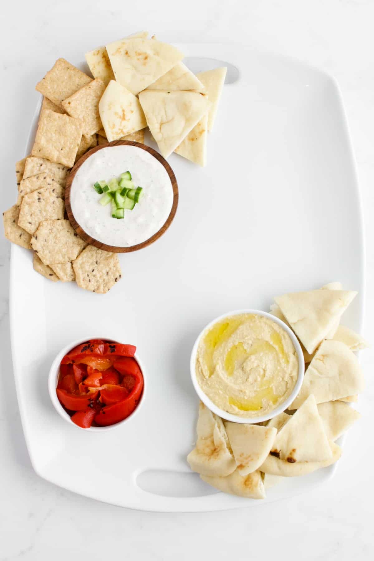 A top view of a Mediterranean charcuterie board in process of being made. The bowls of dips are placed, along with breads and crackers for dipping.