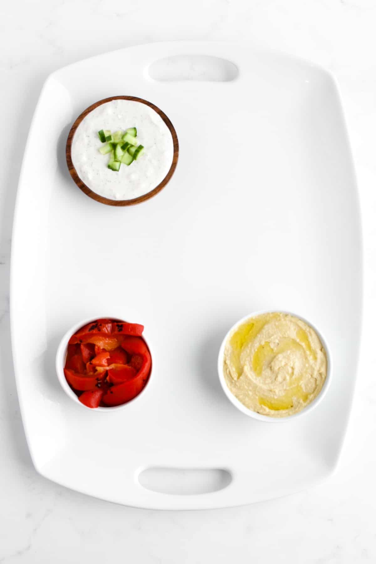 A top view of a Mediterranean charcuterie board in process of being made. The bowls of dips are placed in a triangle on the board.