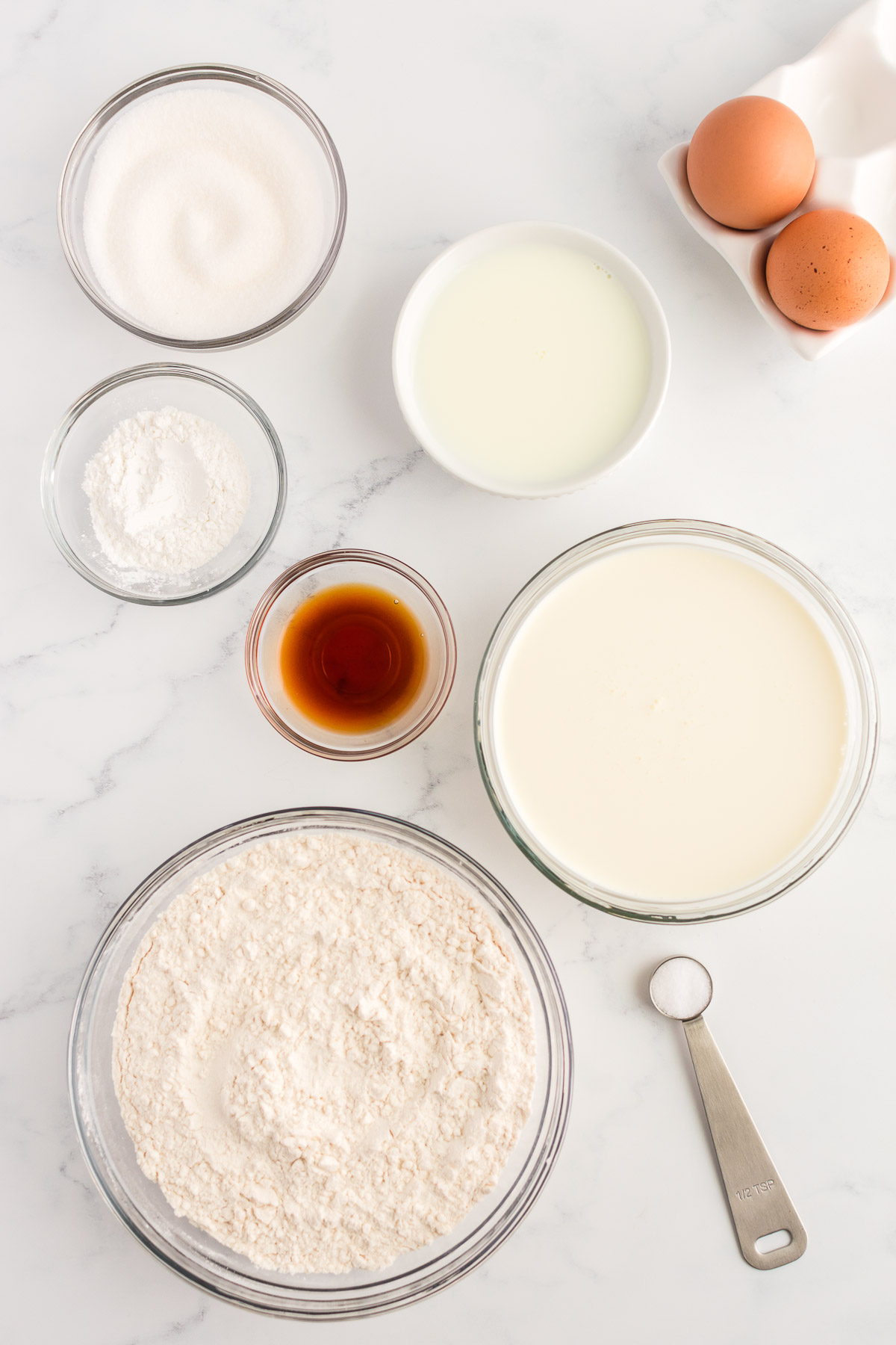 Ingredients for sweet cream pancakes on a marble background.