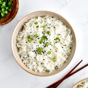 A bowl of coconut basmati rice, garnished with green onions and sesame seeds, with chopsticks to the side.