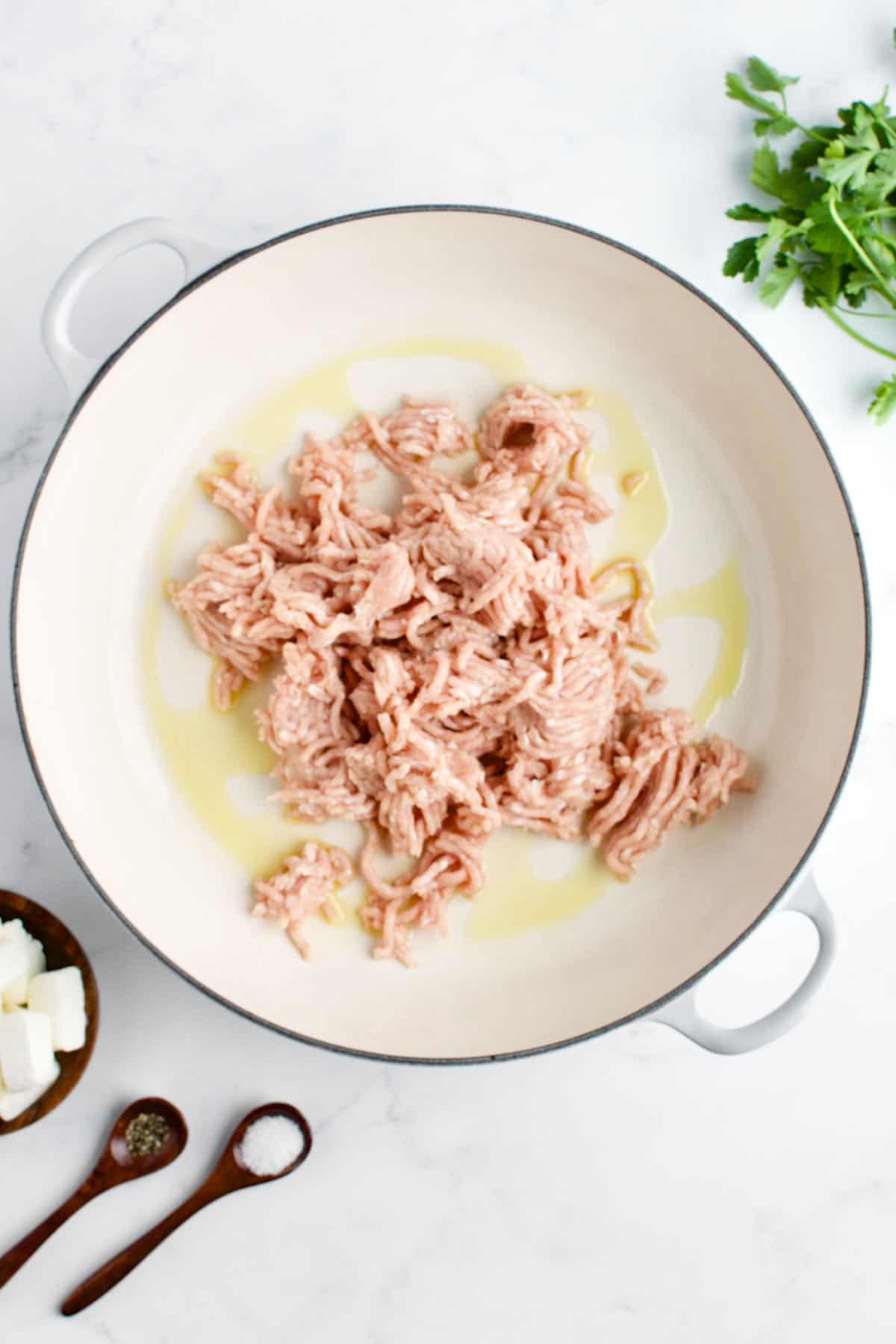 A white skillet with raw ground chicken on a marble background.