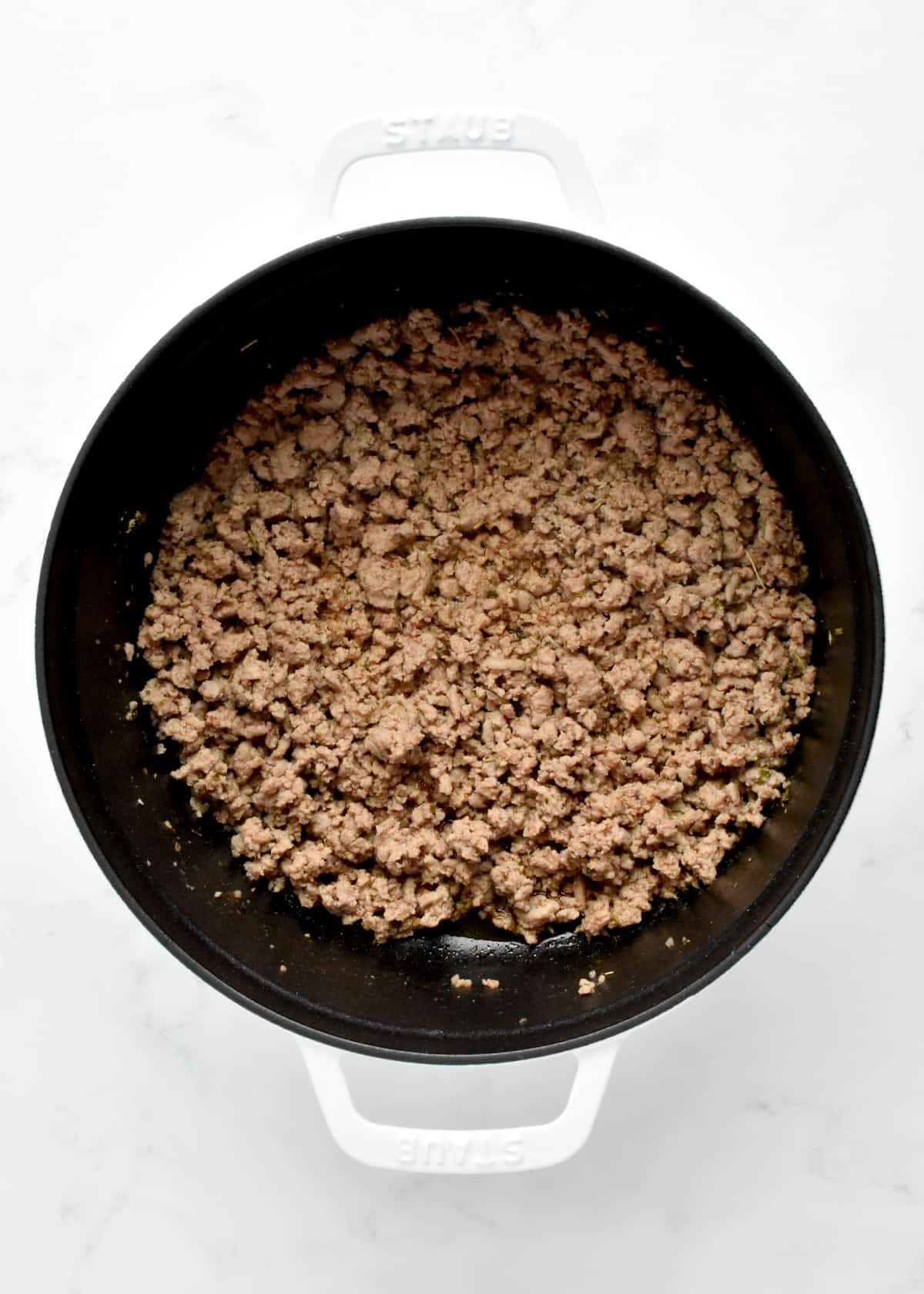 A white dutch oven on a marble background. The pot contains browned ground turkey.