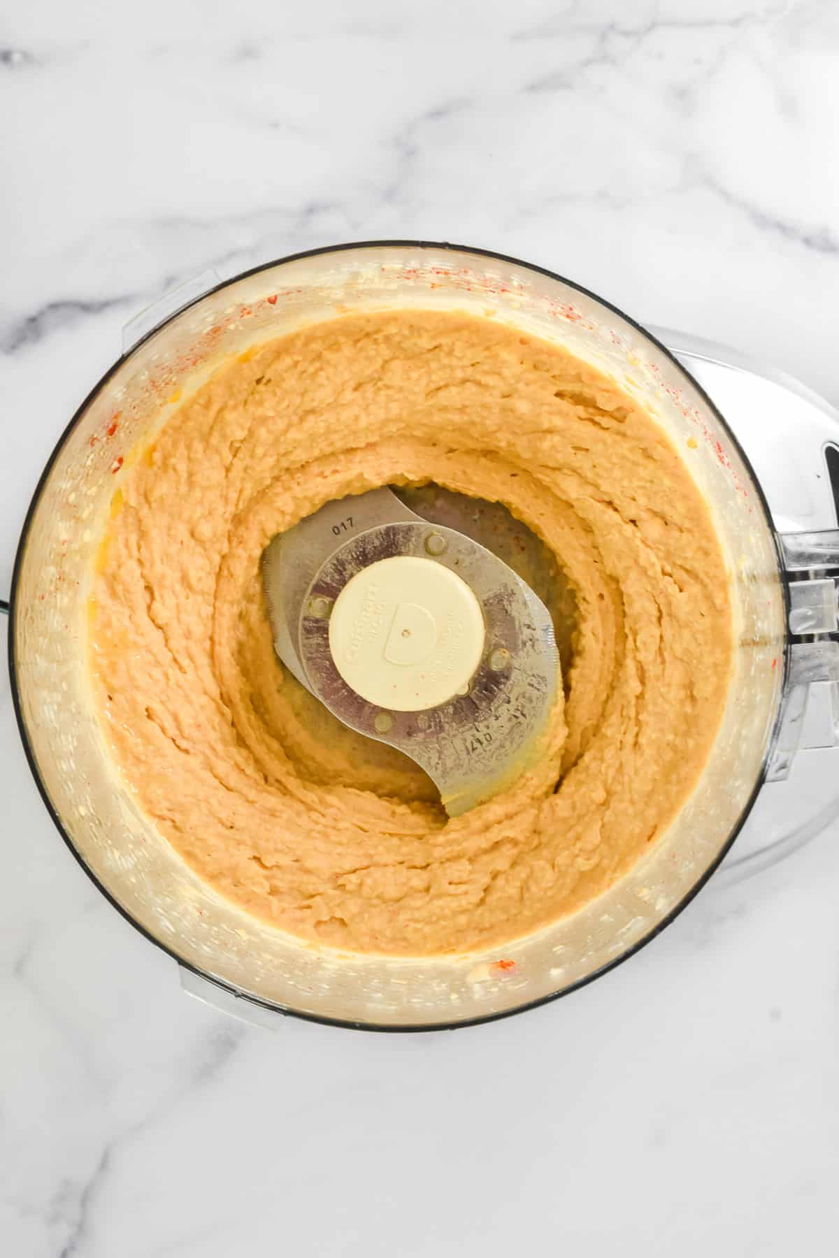 A close up view of the inside of a food process, with ingredients for hummus coarsely blended.