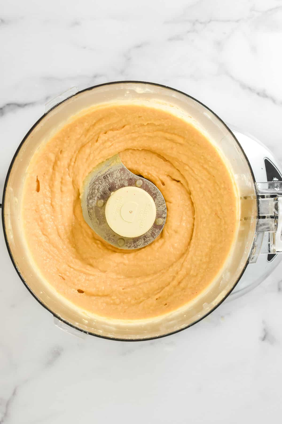 A close up view of the inside of a food process, with smooth creamy hummus.