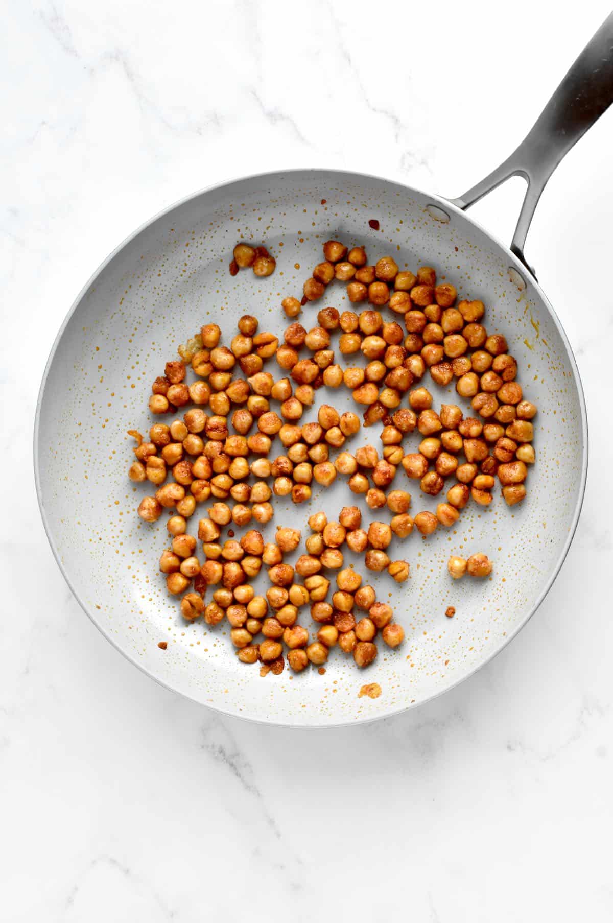 BBQ chickpeas in a grey skillet, on a marble background.